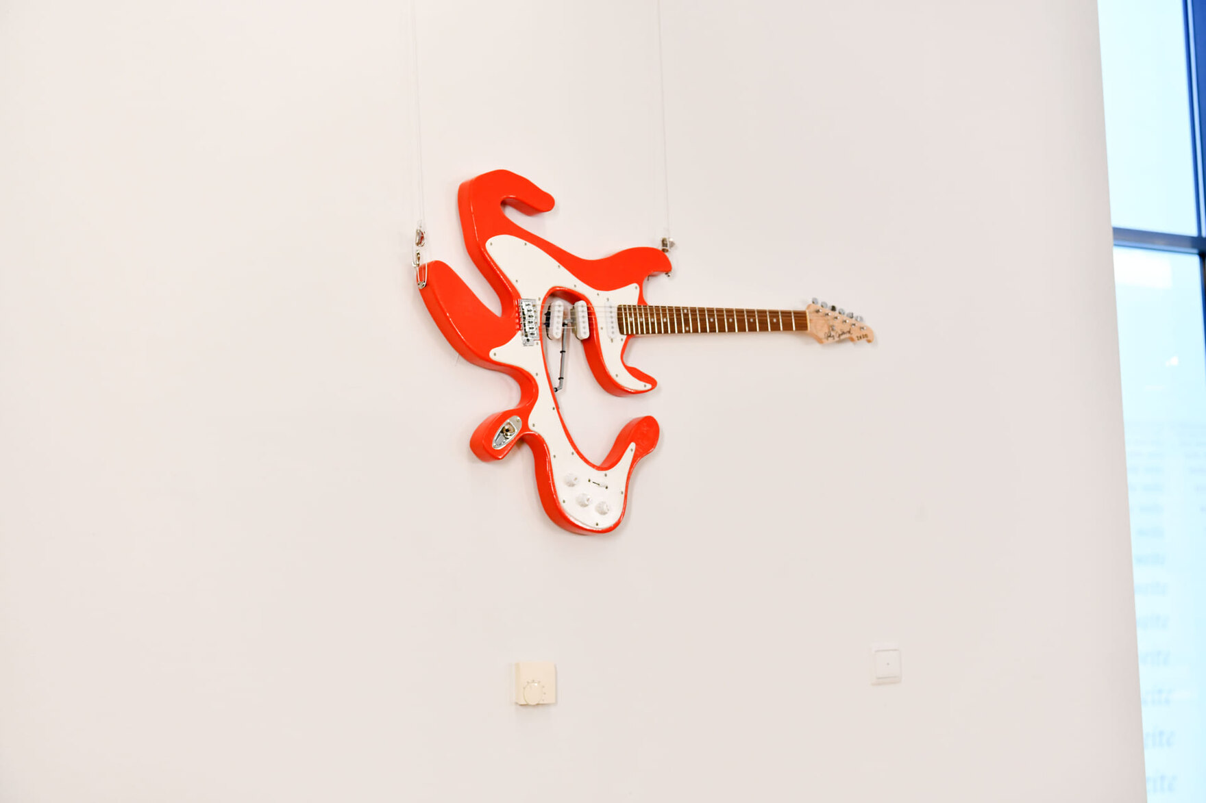 Verformte E-Gitarre als Kunstobjekt hängt an einer weißen Wand
