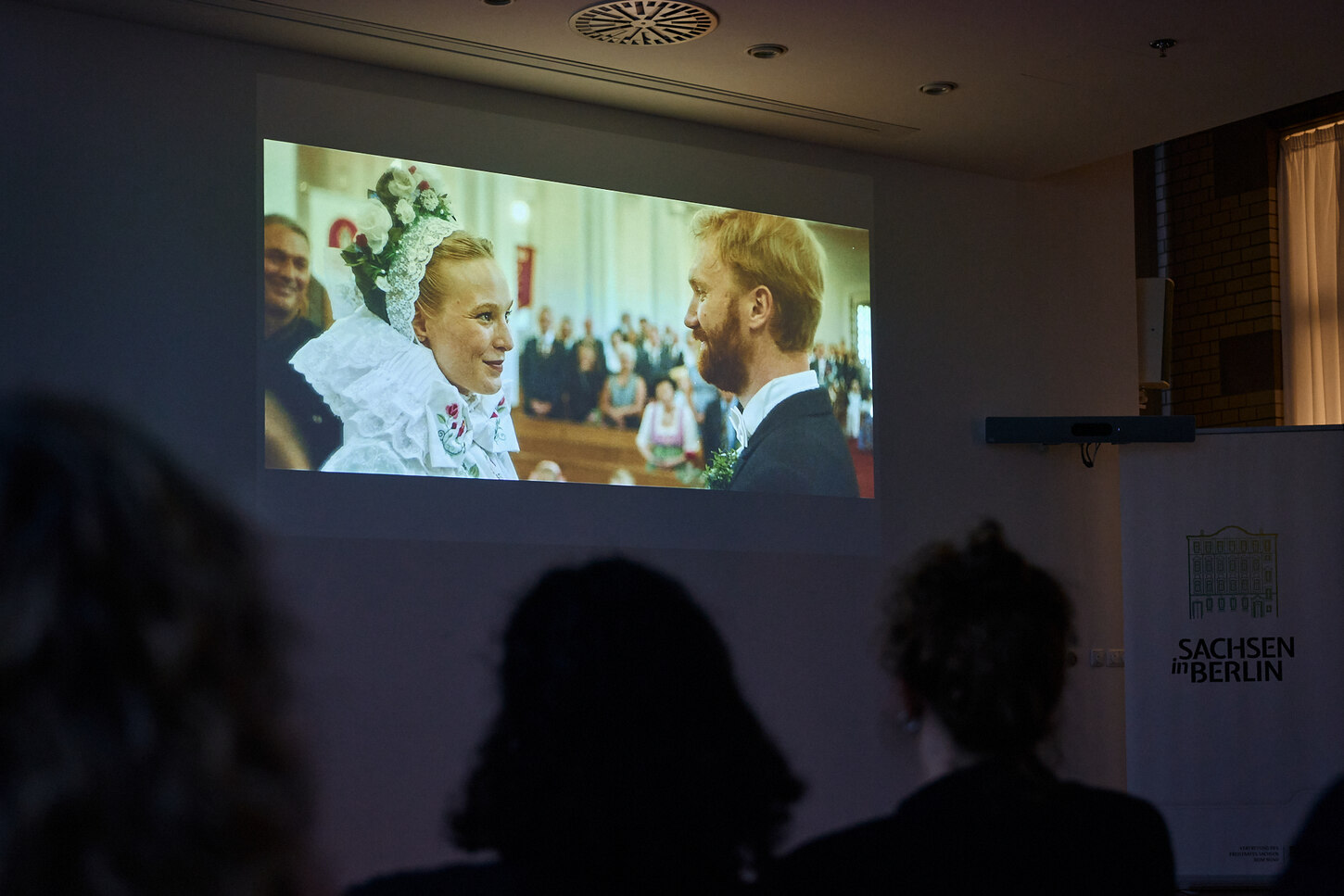Filmszene auf großer Leinwand zeigt ein Paar in sorbischer Hochzeitstracht