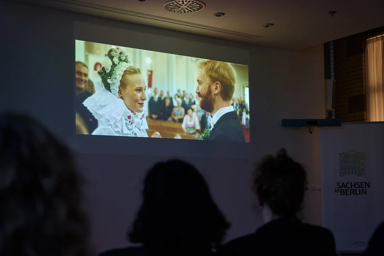 Filmszene auf großer Leinwand zeigt ein Paar in sorbischer Hochzeitstracht