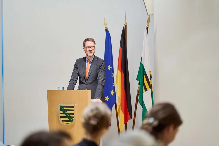 EIn Mann spricht hinter einem Redepult zu einem Publikum.