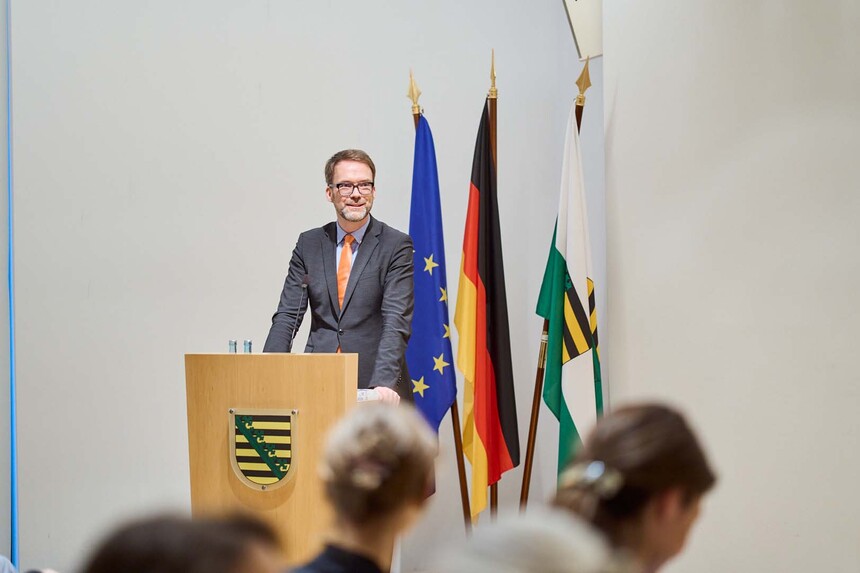 EIn Mann spricht hinter einem Redepult zu einem Publikum.