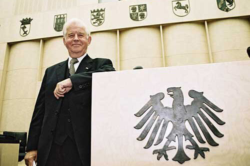 Ein Mann steht neben einem Rednerpult mit dem Bundesadler darauf.