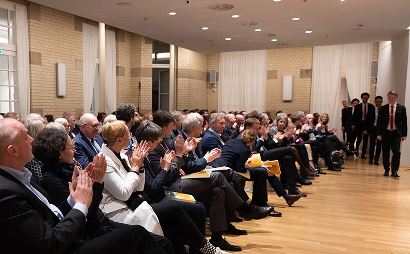 In einem Saal sitzen Menschen, die auf eine Bühne blicken.