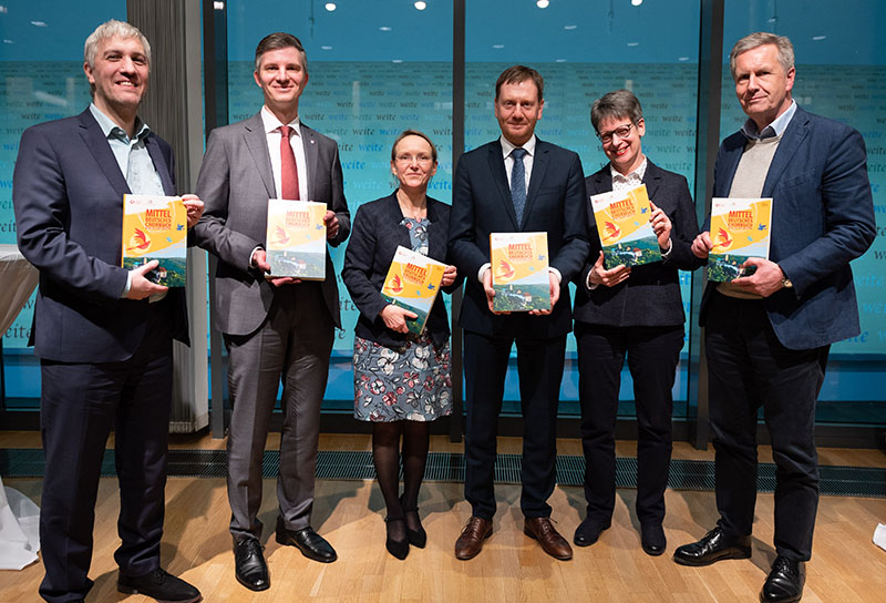 Menschen stehen auf einer Bühne und halten ein Chorbuch in der Hand.