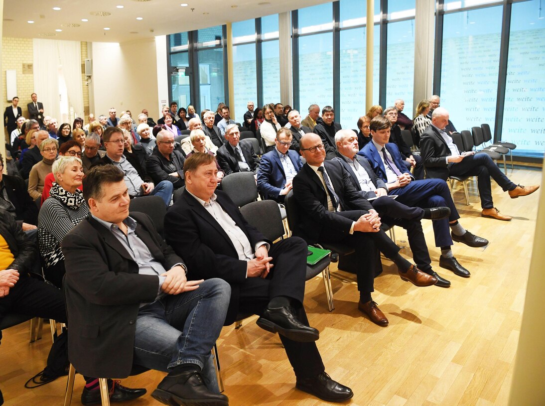 In einem Saal sitzen Männer und Frauen im Publikum.