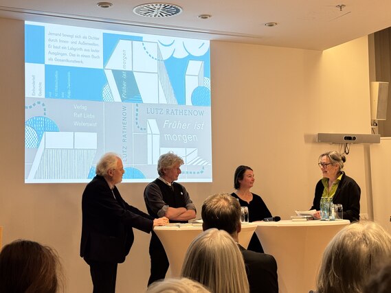 Mehrere Menschen stehen auf einer Bühne hinter Stehtischen.