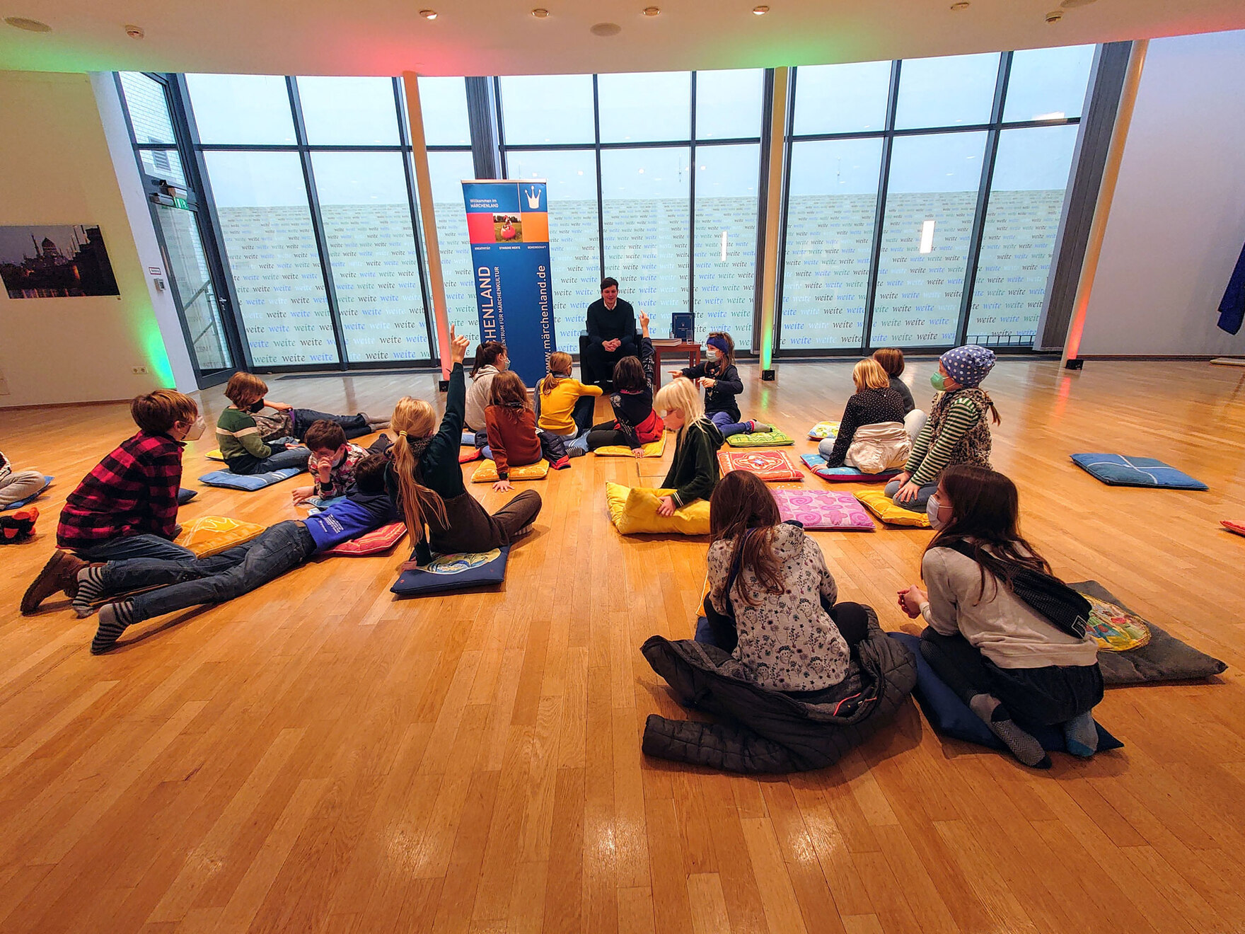 Ein Mann sitzt vor mehreren Kindern, die auf dem Boden sitzen.