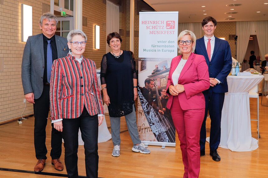 Männer und Frauen stehen in einem Saal und posierenn für ein Foto.